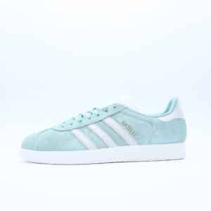 Tenis Adidas Gazelle para mujer. Silueta clásica de perfil bajo en gamuza verde menta con las tres franjas blancas y el icónico grabado dorado.