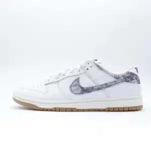 Tenis Nike Dunk Low New Americana piel blanca con estampado de mezclilla azul marino en el logo de Nike y el talón, detalles rojos y suela color caramelo.